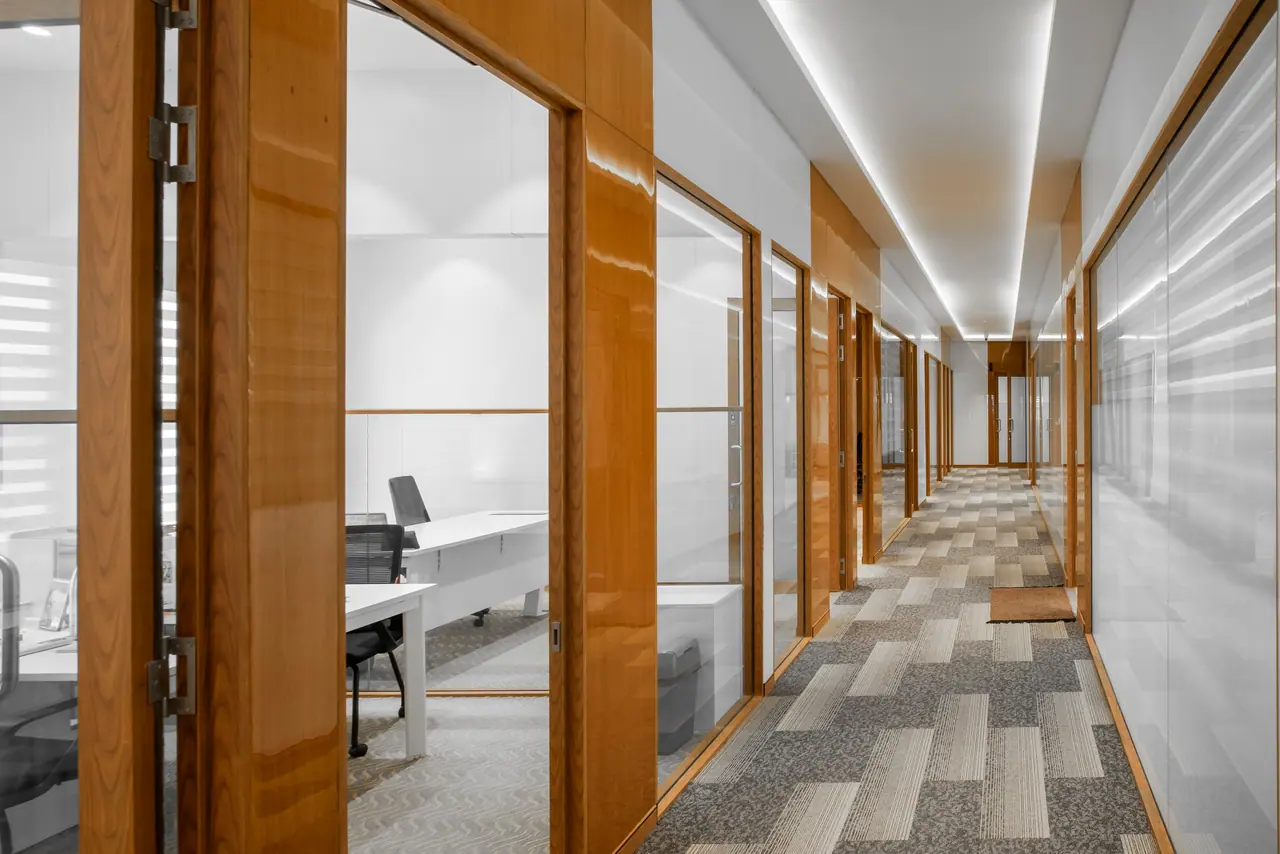 Corridor lined with glass-fronted cabins in gloss wood frames, patterned carpet tiles and a lit ceiling cove