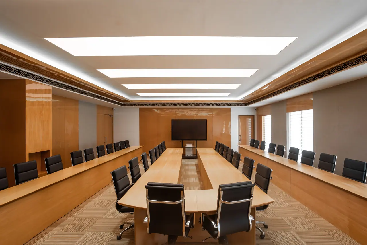 Symmetrical boardroom with a long U-shaped timber table, black leather chairs and backlit ceiling panels
