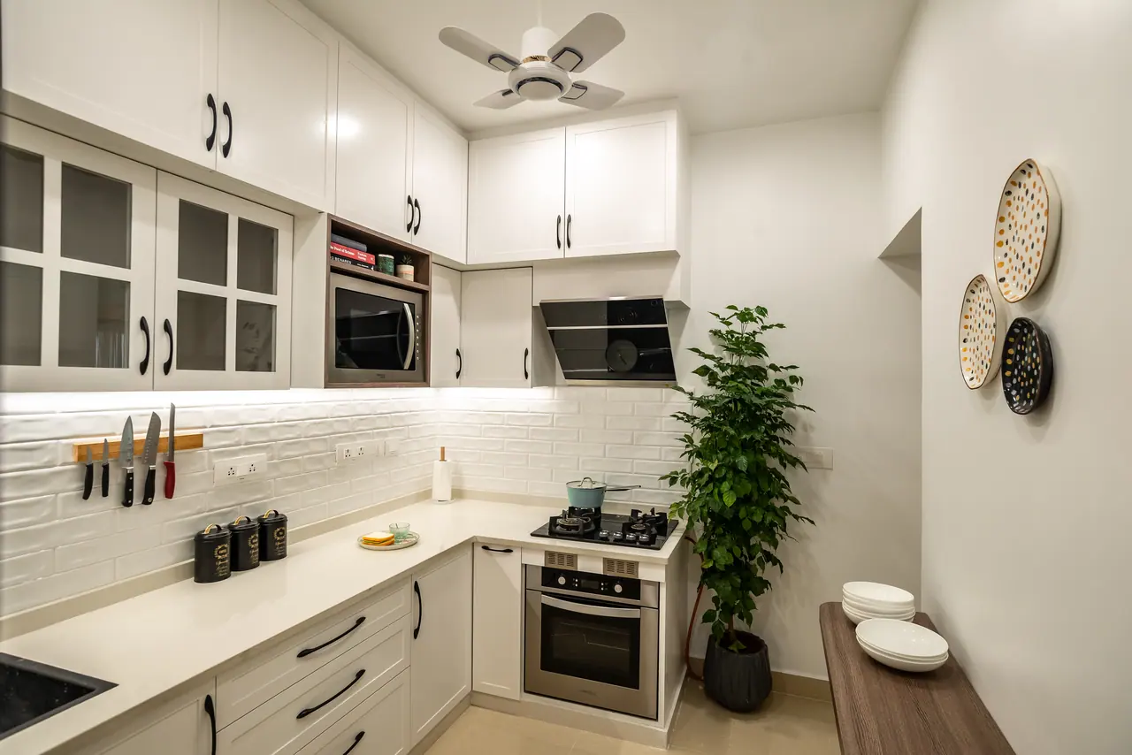 Compact white kitchen with shaker cabinets, subway tile backsplash, built-in oven, gas hob and a potted plant in the corner