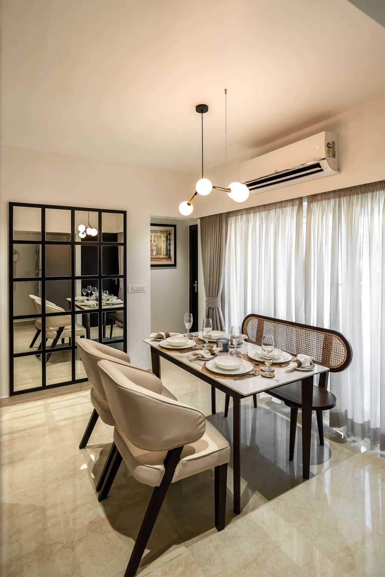 Dining nook with a white marble-look table, cream chairs, a cane-backed bench, a globe pendant and a black grid mirror