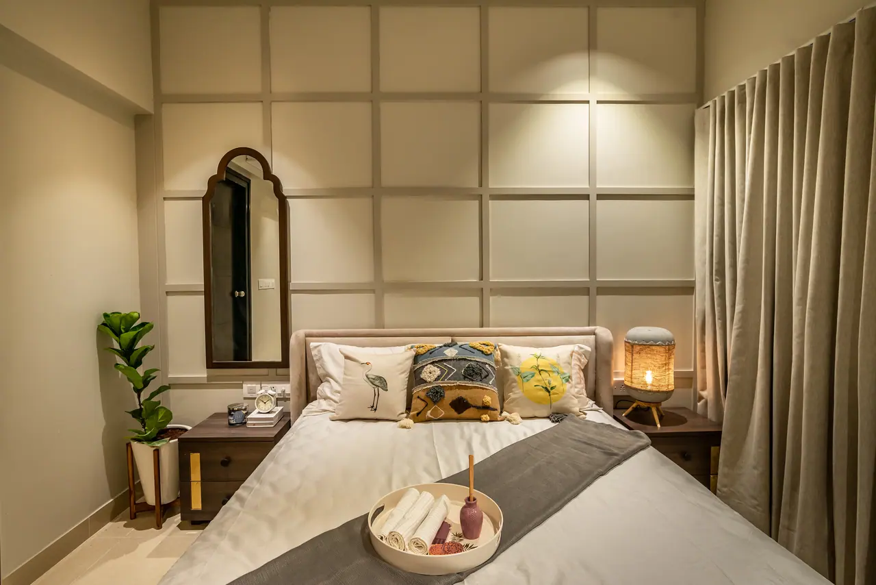 Bedroom with a grid-panelled wall, an arched wooden mirror, an upholstered bed with patterned cushions and a woven lamp