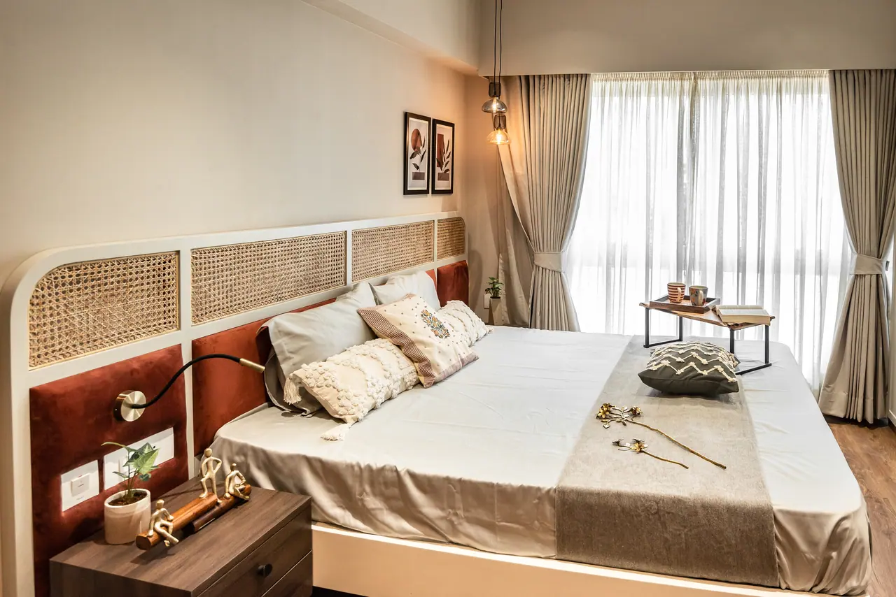 Bedroom with a cane and rust velvet headboard, a flexible reading light, sheer curtains and a bed tray by the window