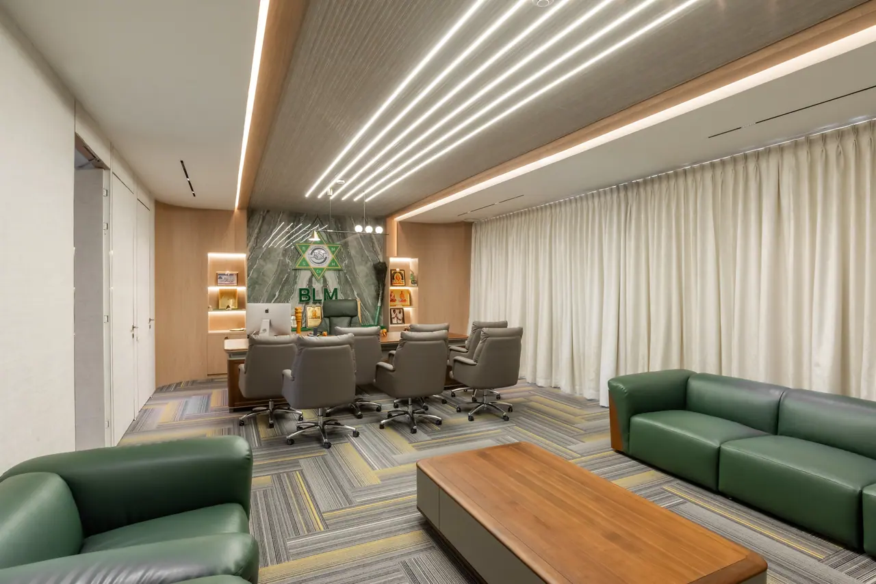 Executive office with green leather sofas, a walnut coffee table and a desk with grey chairs before a green marble wall