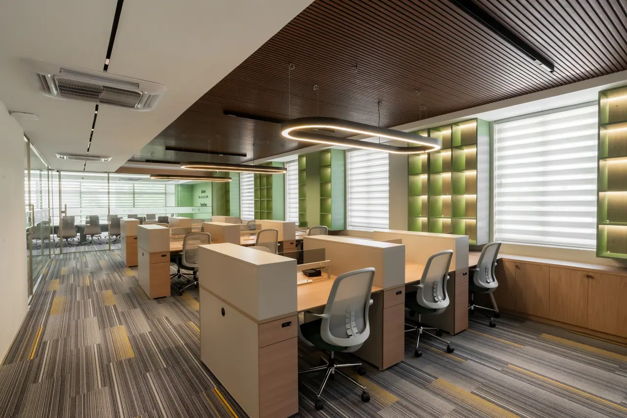 Open-plan workstations with oak storage and mesh chairs under ring pendant lights, a dark slatted ceiling and green shelves
