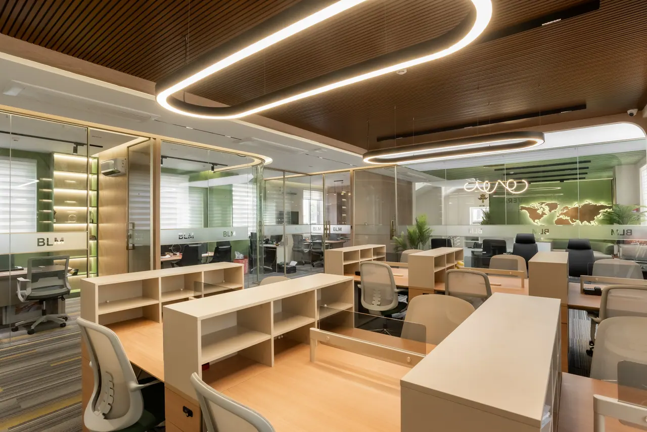 Workstations with oak shelving under oval ring pendants and a slatted wood ceiling, facing a row of glass-walled cabins