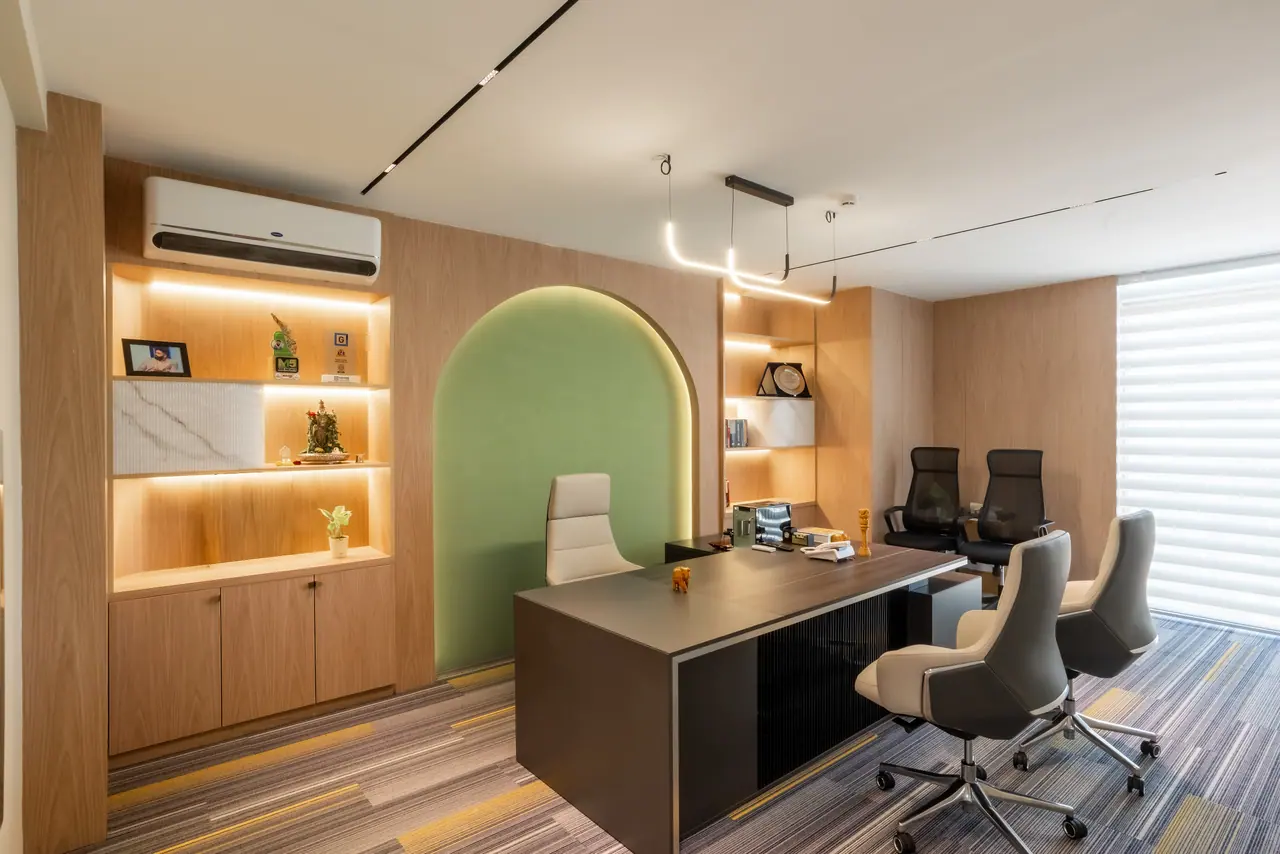 Private office with a dark desk, leather chairs, a lit green arched niche and warm-lit oak shelving under linear lights