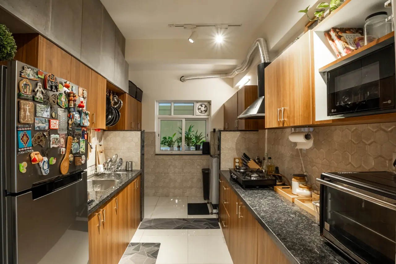 Galley kitchen with wood-finish cabinets, dark granite counters, hexagon-pattern wall tiles and a window lined with plants