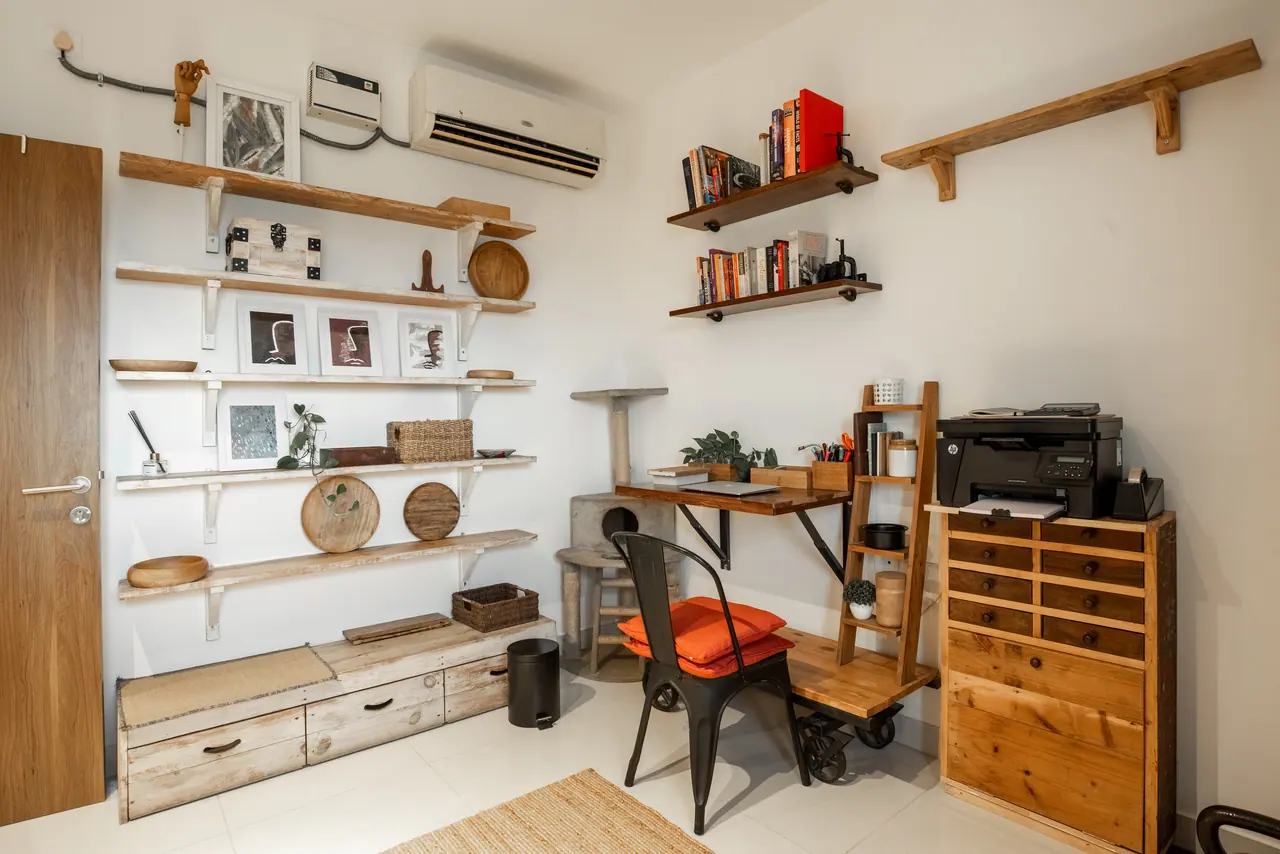 Study with rustic wood wall shelves, a wall-mounted desk, a metal chair with orange cushions and a wooden chest of drawers