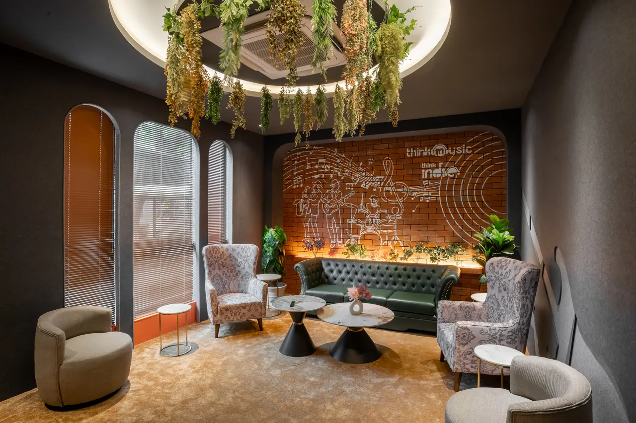 Lounge with patterned wingback chairs, a green chesterfield sofa, arched windows and a brick wall with line art of musicians