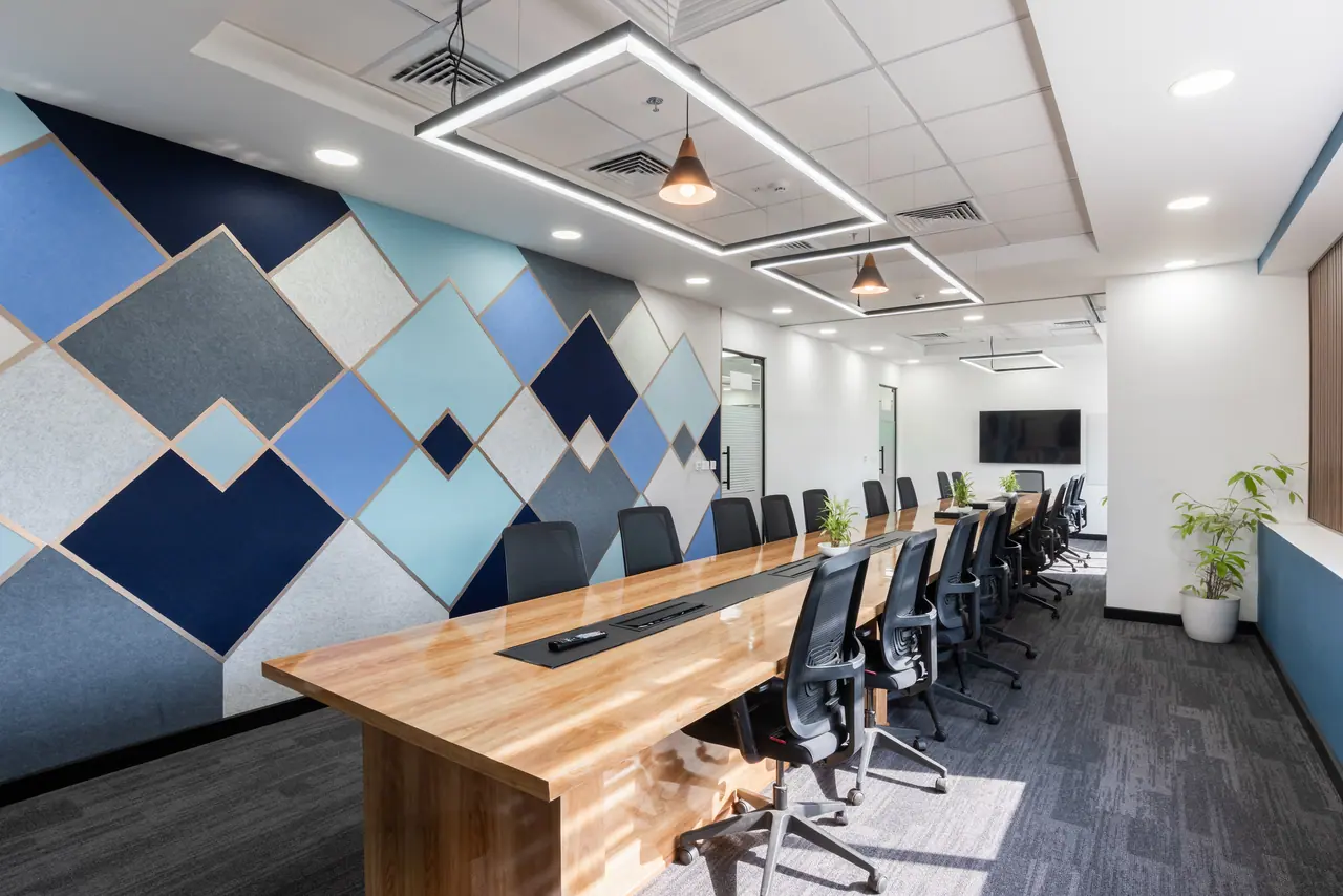 Conference room with a long glossy wood table, mesh chairs, linear light frames and a blue and grey geometric felt wall