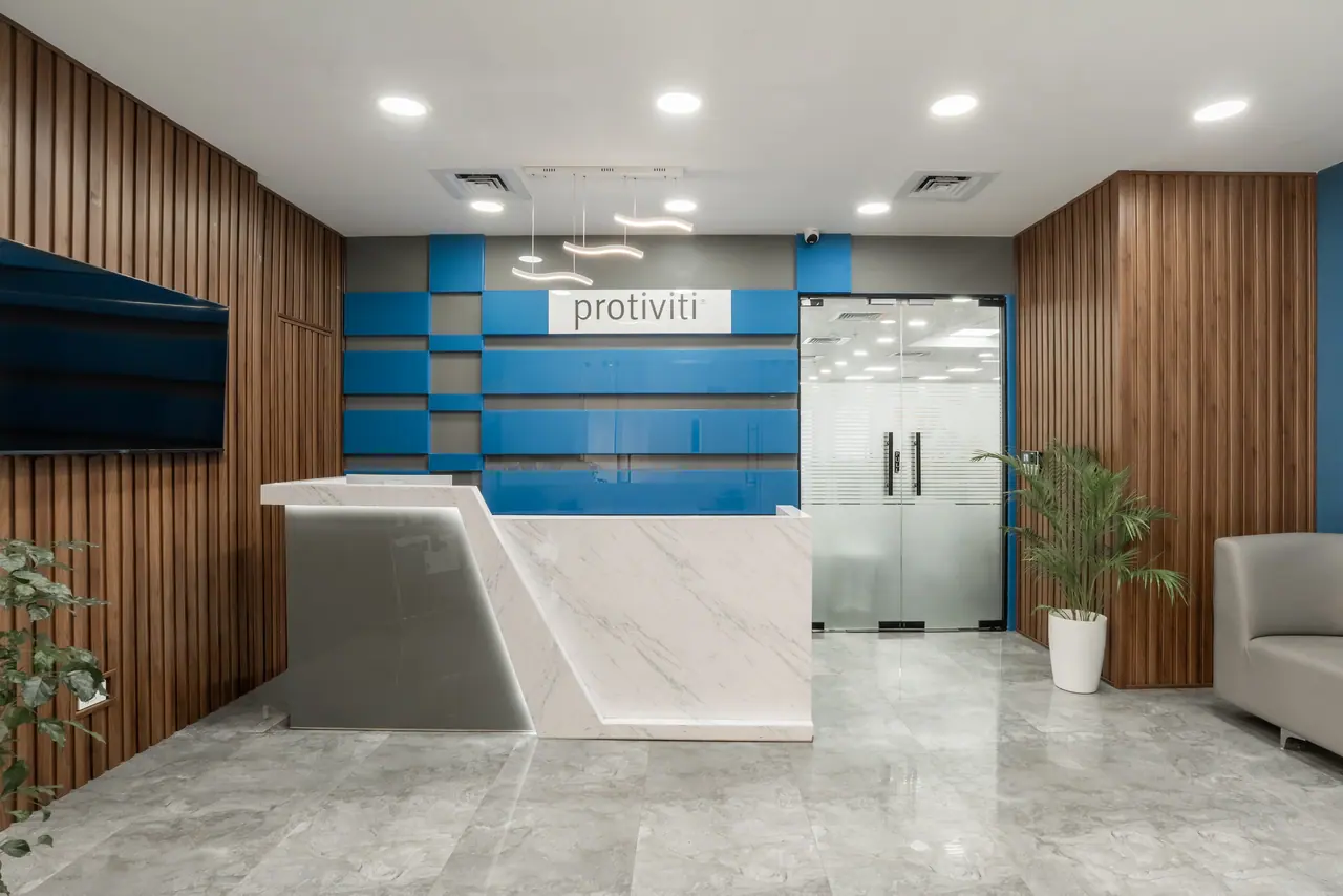 Reception with a white marble-look desk, a blue panelled wall with logo sign, vertical wood slats and frosted glass doors