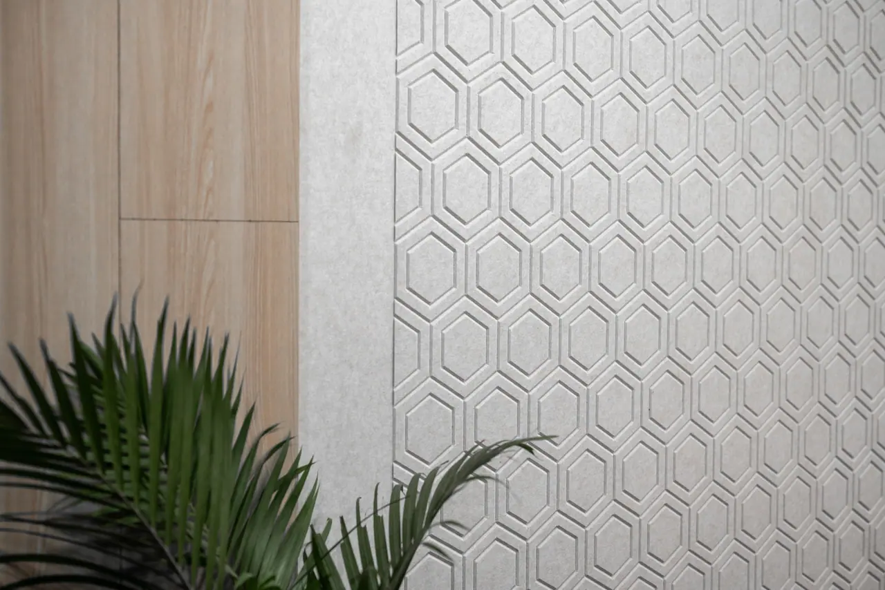 Close-up of a grey embossed hexagon-pattern wall panel beside light wood-grain cladding, with palm fronds in front